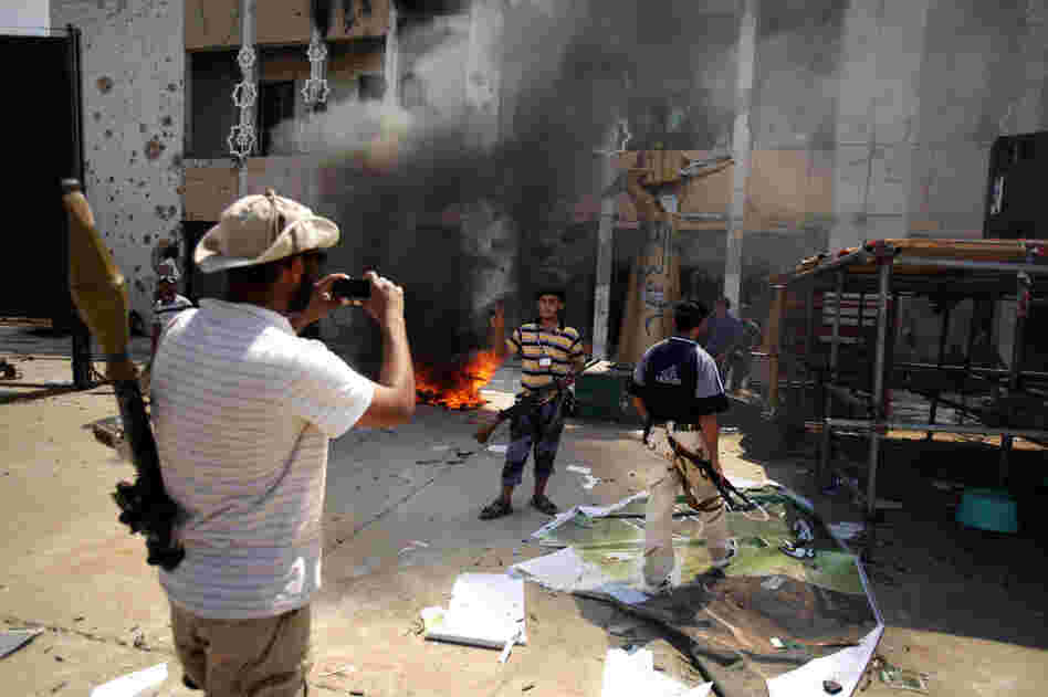 Armed rebels take pictures in front of Gadhafi's heavily damaged compound. 