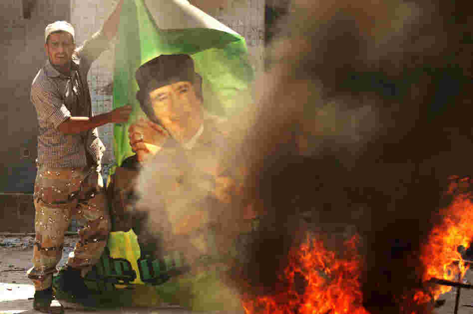A Libyan rebel burns a poster of Gadhafi at the Bab al-Aziziya compound. 