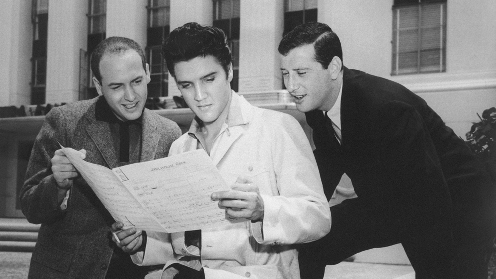 Jerry Leiber (right) looks over Elvis Presley's shoulder at the sheet music for "Jailhouse Rock" in Los Angeles in 1957. His songwriting partner Mike Stoller stands to the left.