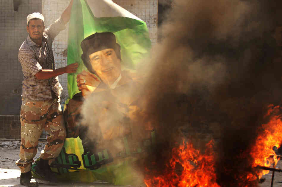 A Libyan rebel burns a poster of Gadhafi at the Bab al-Aziziya compound. 
