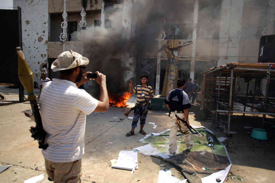 Armed rebels take pictures in front of Gadhafi's heavily damaged compound. 