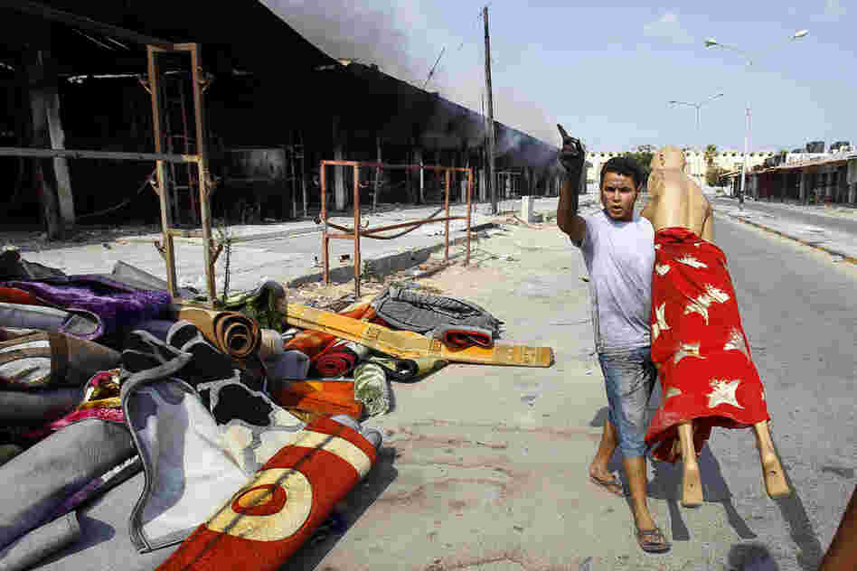 After an intense battle in the Abu Salim district of Tripoli, a man removes a mannequin from a clothes shop. 