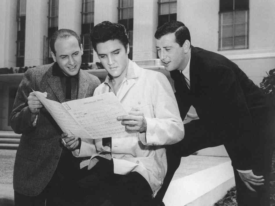 Jerry Leiber (right) looks over Elvis Presley's shoulder at the sheet music for "Jailhouse Rock" in Los Angeles in 1957. His songwriting partner Mike Stoller stands to the left.