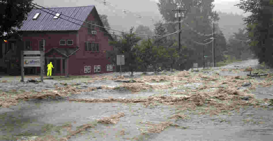 A person checks a building for occupants as raging floodwaters cross Route 100, closing the main road in Waitsfield, Vt., on Sunday. 