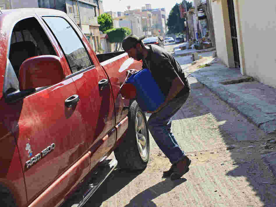 A man pours gas into the tank of his car in Tripoli on Saturday. Residents in the Libyan capital are scrambling to get basic supplies, such as fuel and water.