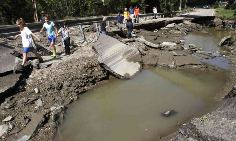 People walk along a washed out section of Route 12 on Monday in Berlin, Vt.