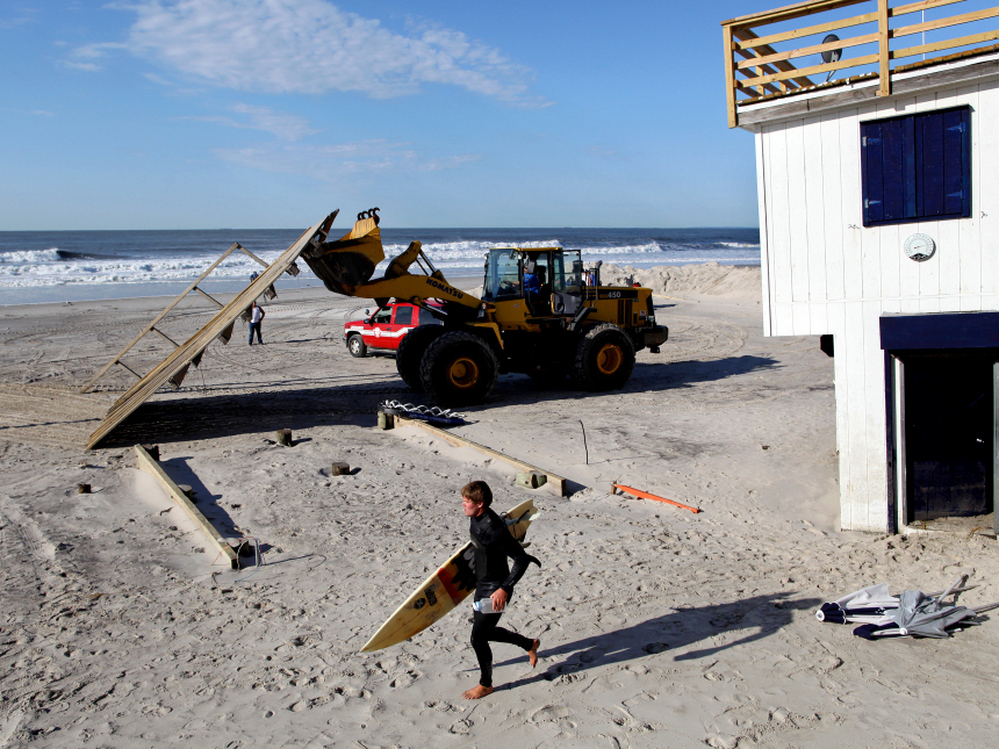 A surfer in Long Beach, N.Y., passes heavy machinery Monday that was removing the remnants of a lifeguard shack that was knocked off its footing during Irene.