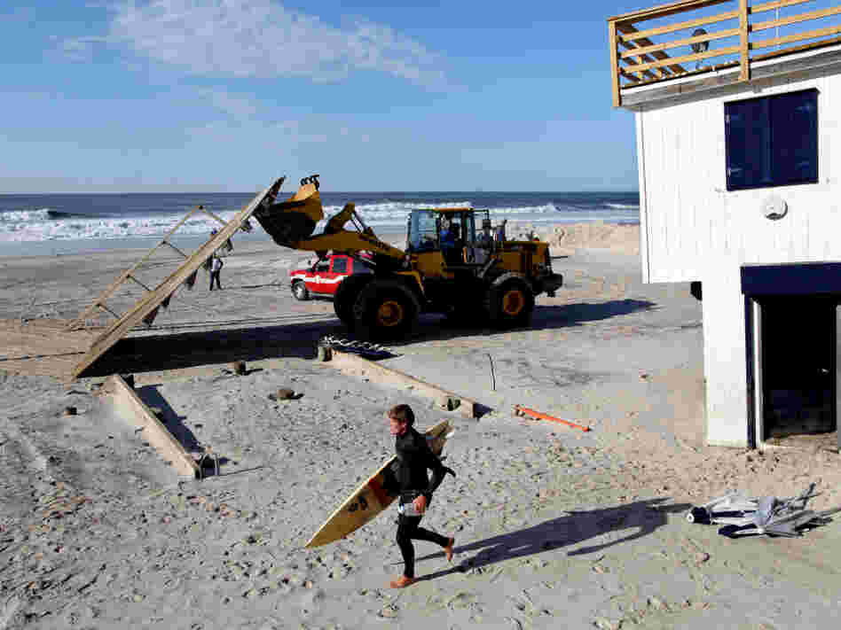 A surfer in Long Beach, N.Y., passes heavy machinery Monday that was removing the remnants of a lifeguard shack that was knocked off its footing during Irene.