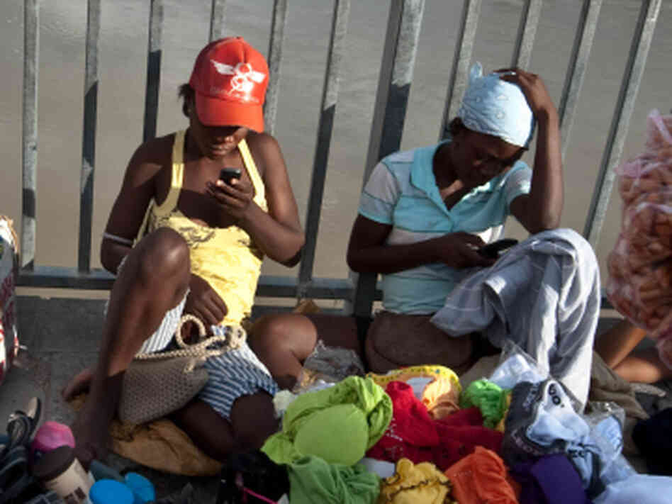 Two women check their cellphones as they hawk their wares on a bridge over the Artibonite River, whose waters are  believed to be the source of Haiti's 2010 cholera outbreak.