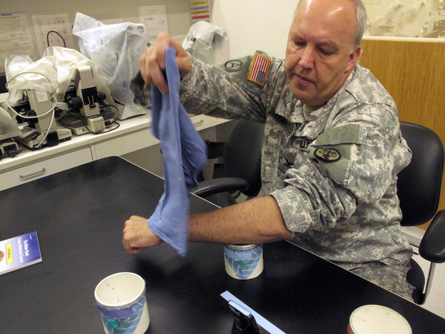 Col. Christian Ockenhouse, director of malaria vaccine research at Walter Reed Army Institute of Research, shows how volunteers are infected with malaria — by holding their forearms over a container holding five malaria-infected mosquitoes. The container is covered with a mesh, allowing the mosquitoes to bite the volunteers.