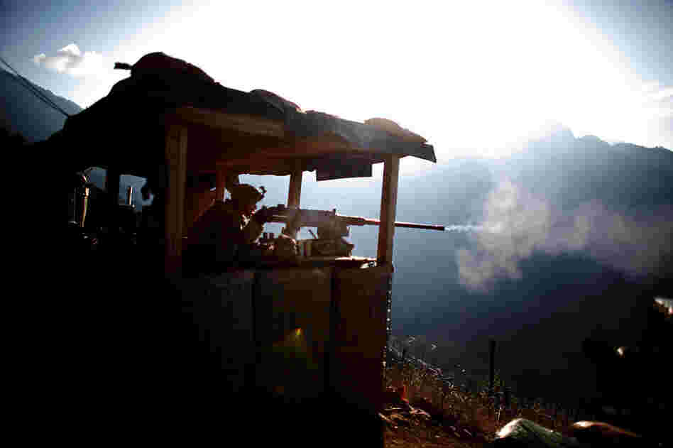 Pfc. Martinez fires a machine gun at an enemy fighting position, while insurgents fire at another American base in the valley bellow.