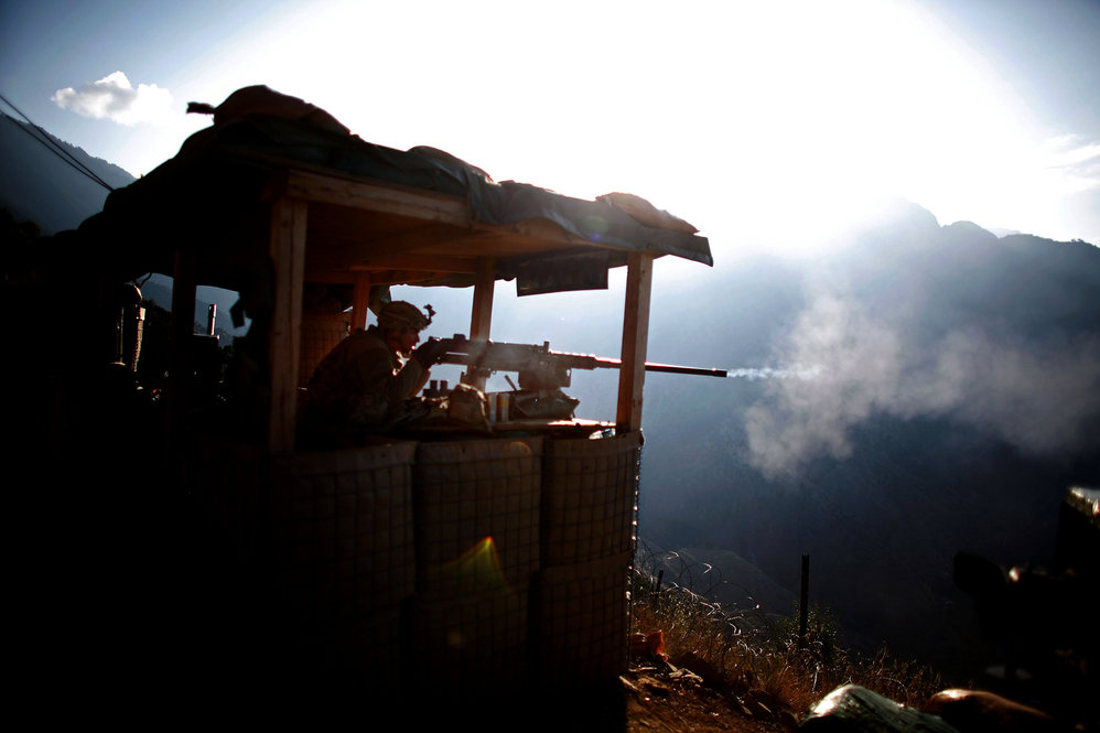 Pfc. Martinez fires a machine gun at an enemy fighting position, while insurgents fire at another American base in the valley bellow.