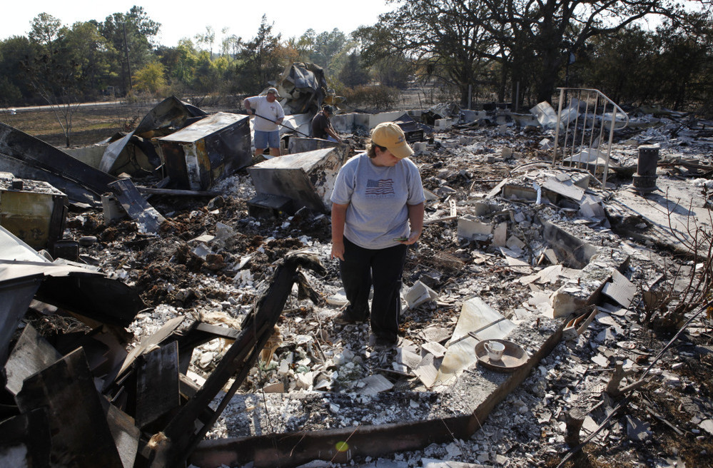 Hillary Polly looks through the family belongings as Thomas Polly tries to pry open a fireproof gun safe with his father Louie Polly in the background amongst the rubble of their burned house near Bastrop, Texas.