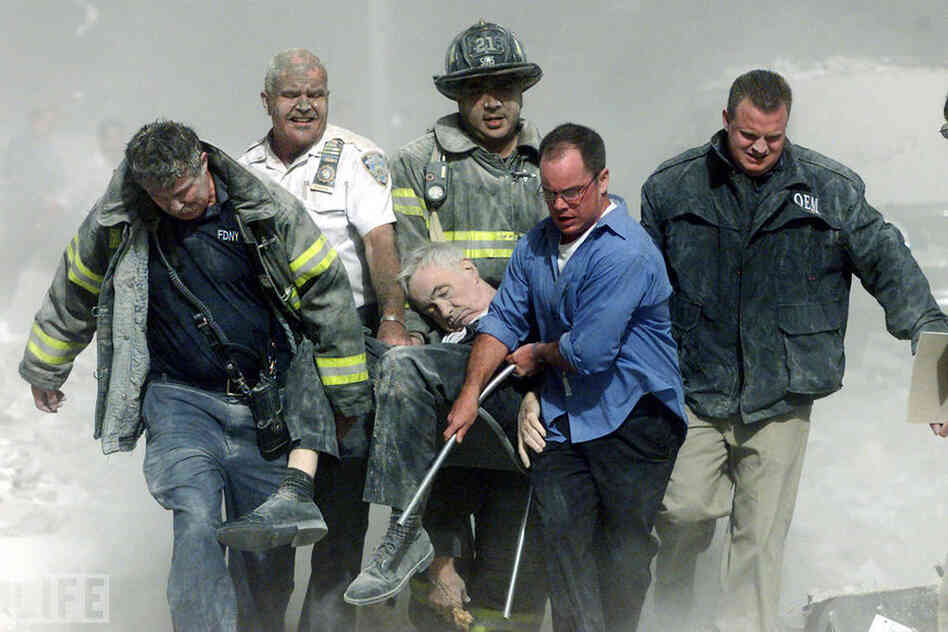 Rescue workers carry mortally injured New York City Fire Department chaplain Mychal Judge from the wreckage after he was killed by falling debris while administering last rites to another victim. A Roman Catholic priest, a recovering alcoholic, a gay man, and a spiritual adviser and trusted friend to countless firefighters through the years, "Father Mike" was the first recorded victim of the Se...