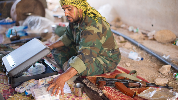 A fighter loyal to the Transitional National Council sits with money that has been donated to pay fighters at a checkpoint outside Bani Walid, Libya, on Monday. It was widely feared that ousted leader Moammar Gadhafi and his supporters spirited away much of the country's wealth. But those fears have yet to materialize, as Libya's central bank holdings appear to remain largely intact.