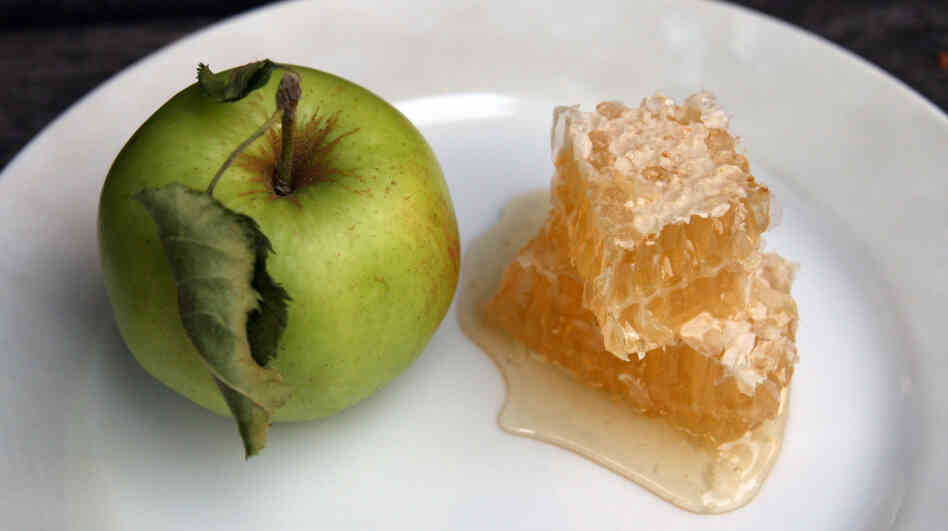 A small green apple next to a stack of honeycomb chunks on a plate