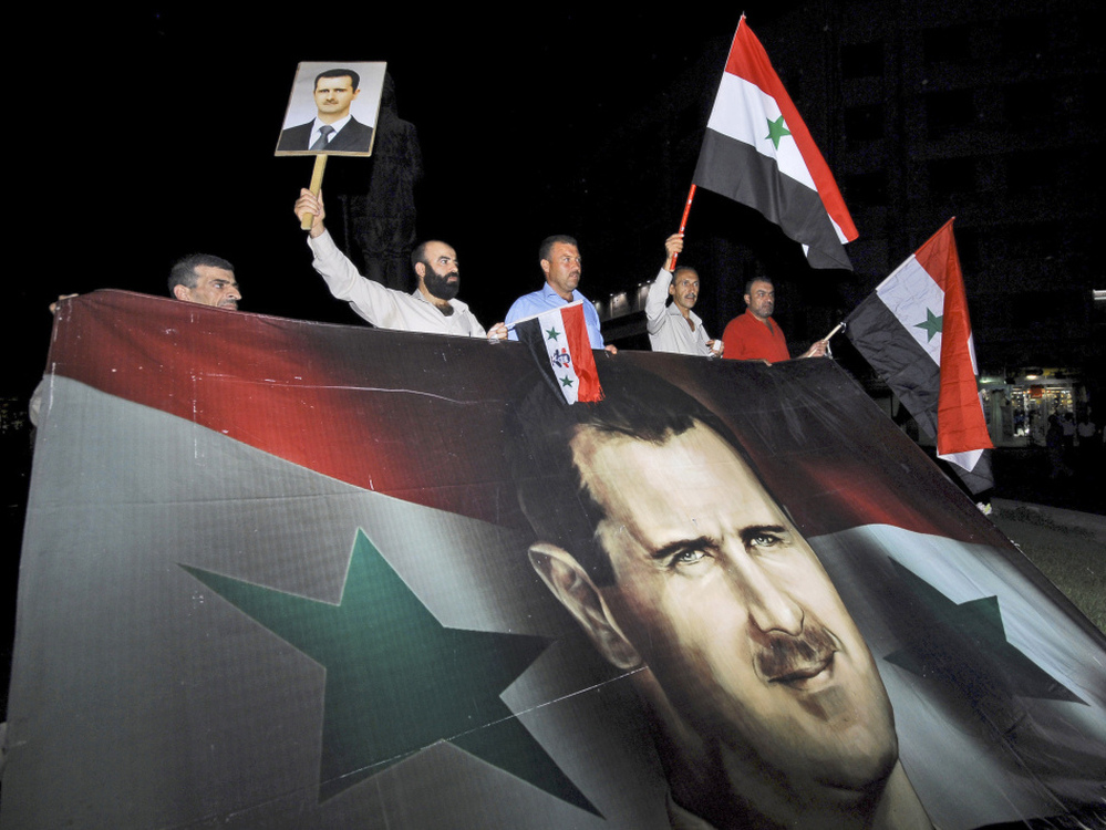 Supporters of Syrian President Bashar Assad carry a giant flag with his image on it during a pro-regime protest in Damascus, Syria, in August. Pro-government forces are now taking their message to a new arena: cyberspace.