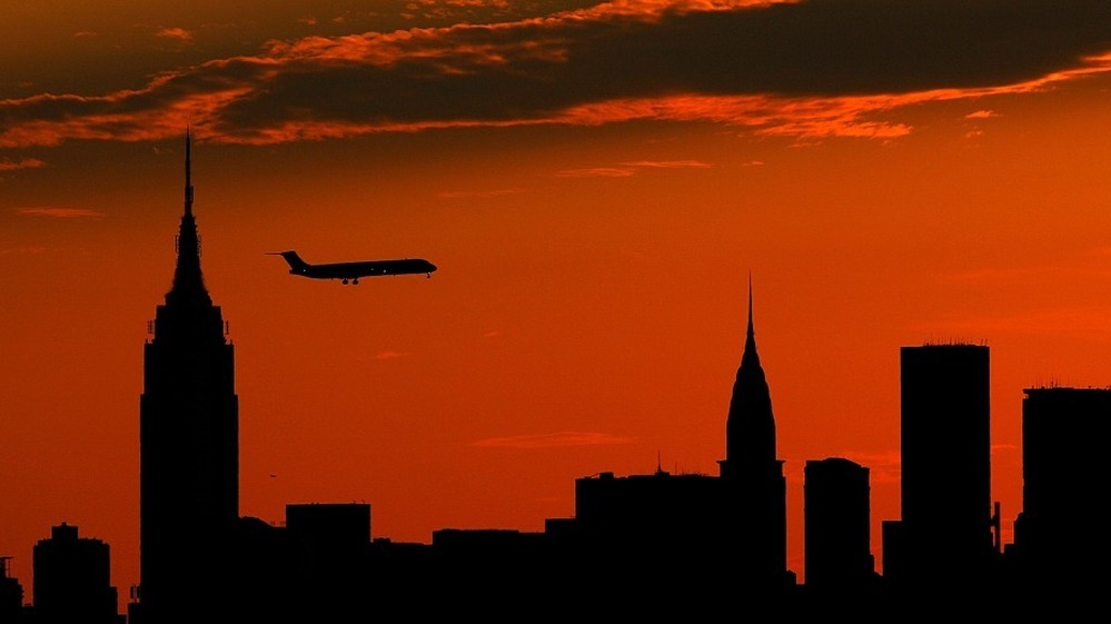 A plane flies past the Manhattan skyline at sunset.