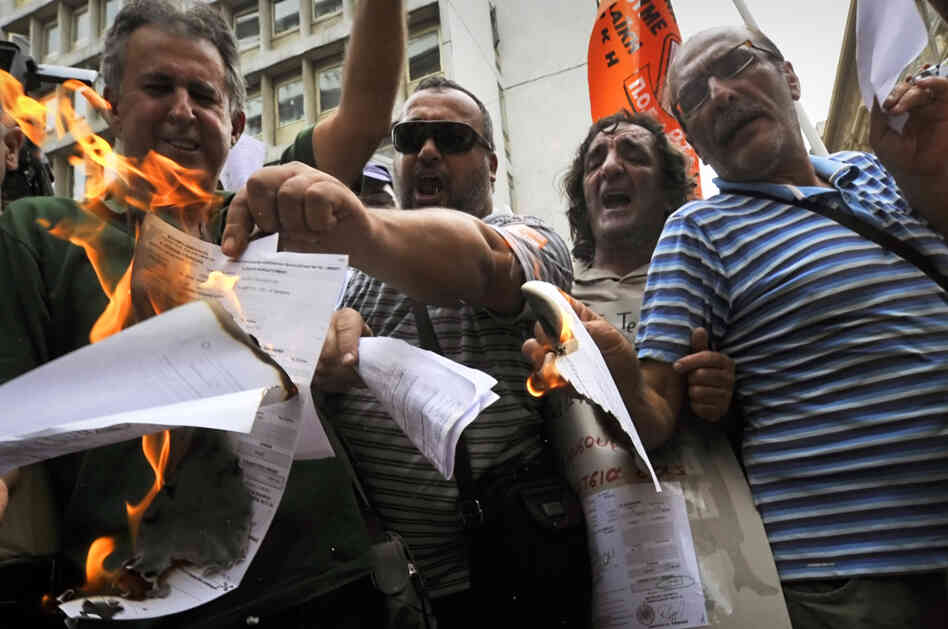 Greek public sector employees burn their tax notices outside the Finance Ministry in Athens last week. Greek public sector employees burn their tax notices outside the Finance Ministry in Athens last week.