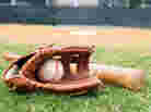 Old baseball, glove, and bat on field with base and outfield in background.