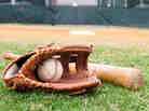 Old baseball, glove, and bat on field with base and outfield in background.