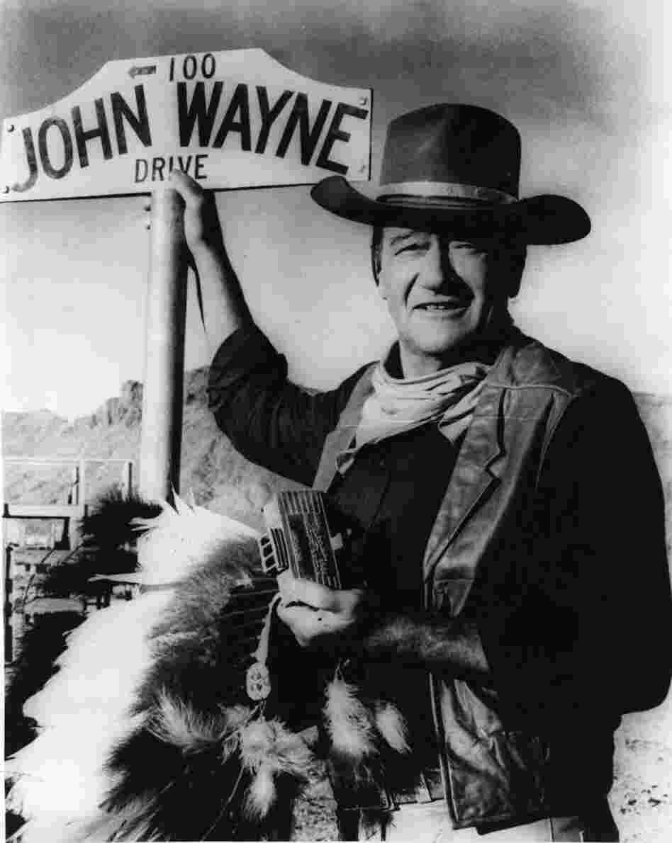 American actor John Wayne stands by the street sign honoring his name in Prescott, Ariz. The film star "was one of the defining Americans of the 20th century," says critic John Powers.