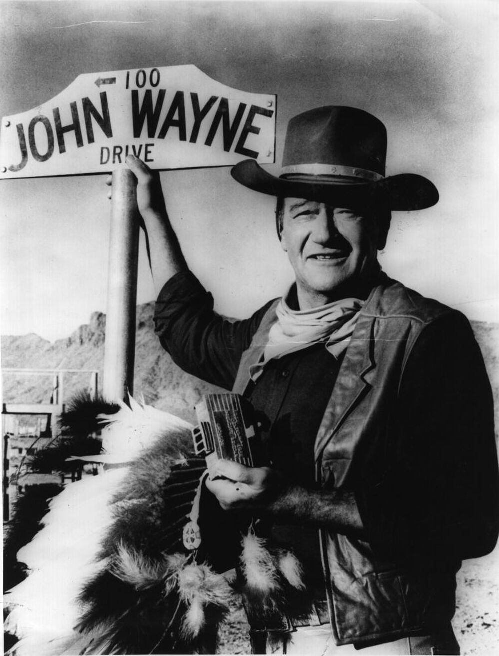 American actor John Wayne stands by the street sign honoring his name in Prescott, Ariz. The film star "was one of the defining Americans of the 20th century," says critic John Powers.