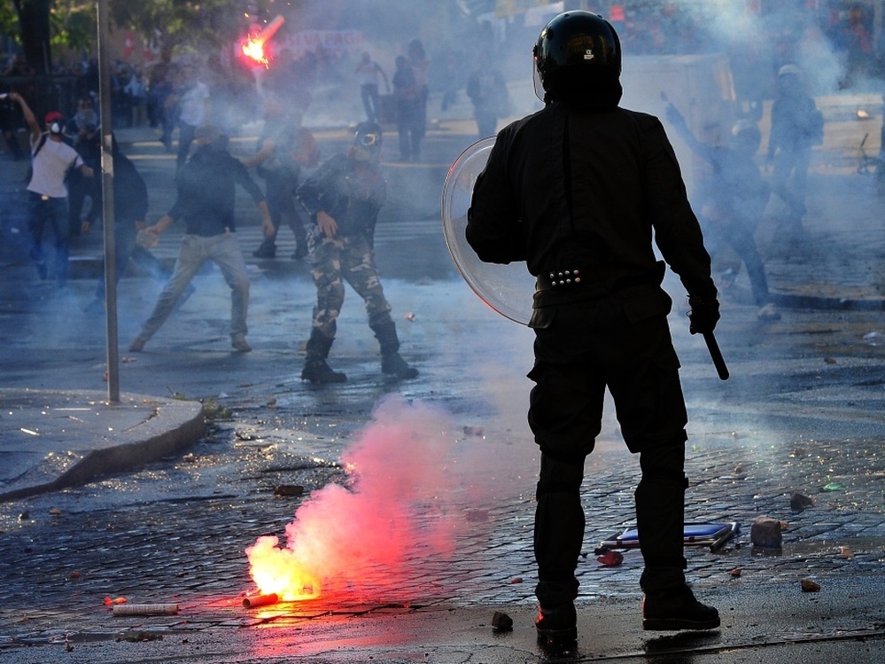 An anti-riot police officer stands as protesters launch flares in Rome after a demonstration turned into a riot Saturday.