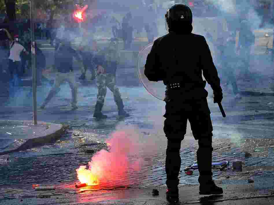 An anti-riot police officer stands as protesters launch flares in Rome after a demonstration turned into a riot Saturday.