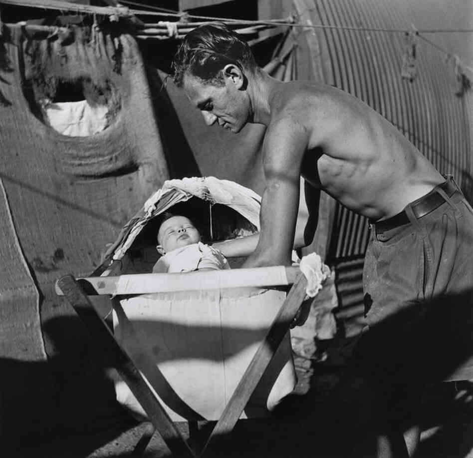 A father puts his baby to sleep in a bassinet constructed from gathered rags and pieces of wood, Cyprus Internment Camp, 1947