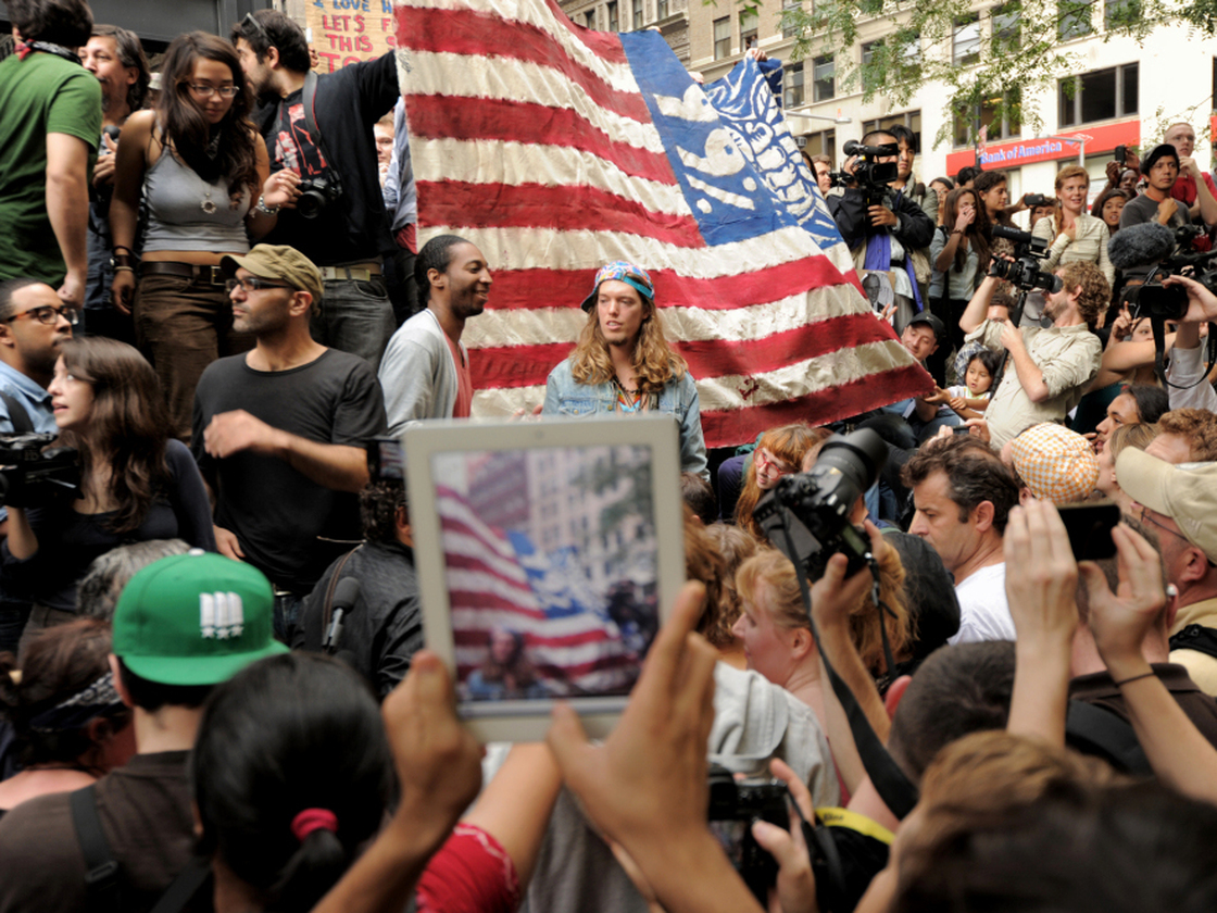 An onlooker takes a photograph of Occupy Wall Street protesters in New York's Zuccotti Park. The demonstrations were inspired by a blog post by Kalle Lasn, founder of Adbusters magazine.