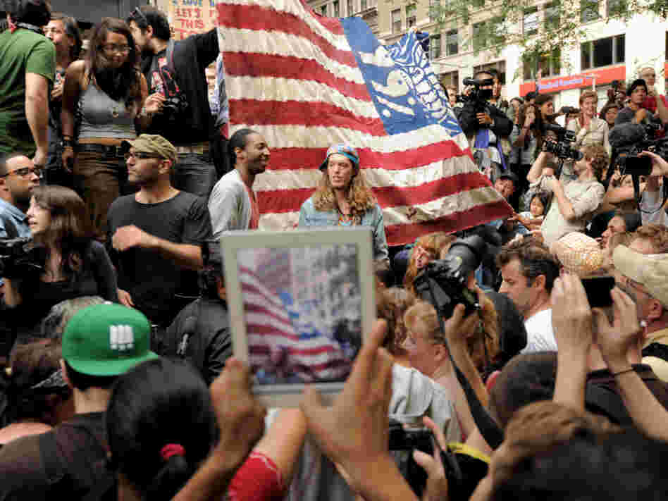 An onlooker takes a photograph of Occupy Wall Street protesters in New York's Zuccotti Park. The demonstrations were inspired by a blog post by Kalle Lasn, founder of Adbusters magazine.