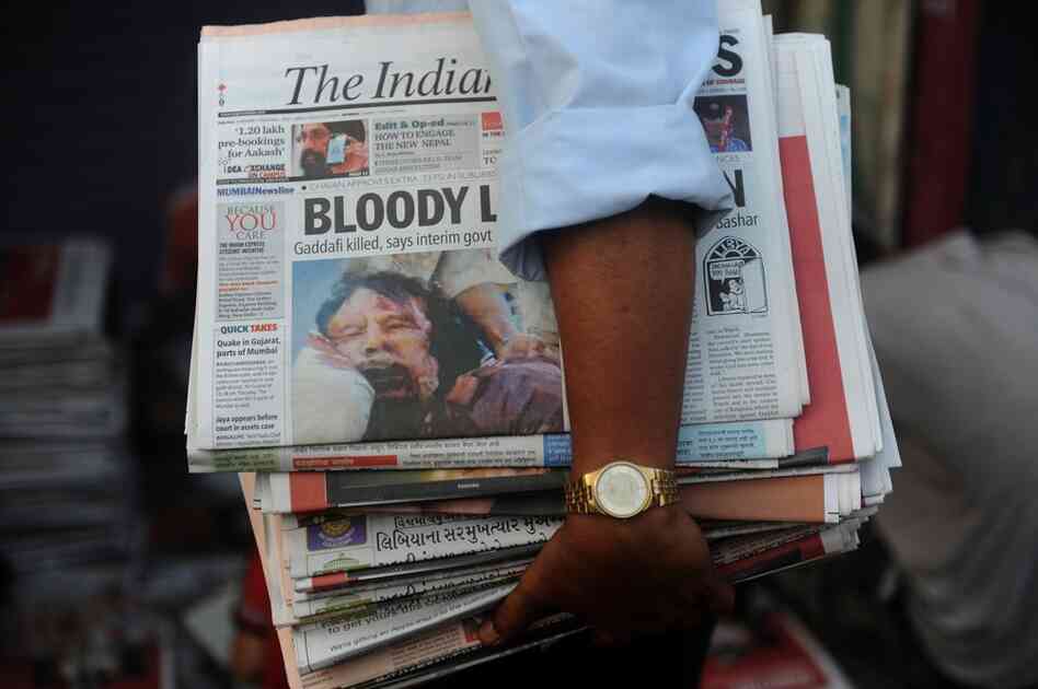 A vendor distributes papers with the news of Moammar Gadhafi's death in Mumbai on Friday. 