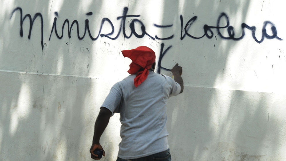 A Haitian protester in Port-au-Prince last month spray-paints a wall, equating the UN mission in Haiti (abbreviated here as MINISTA) with cholera. 