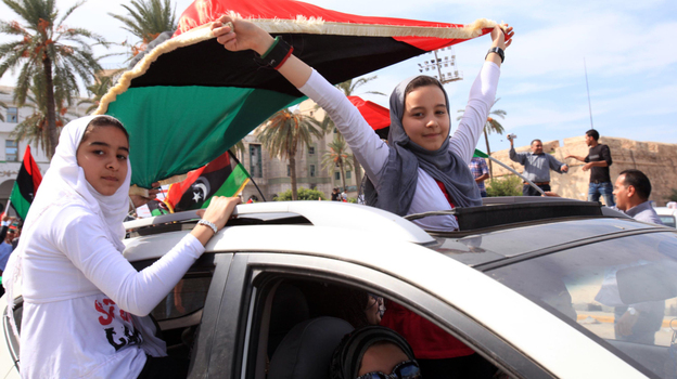 Libyan girls wave flags of the Transitional National Council as they ride through the streets of Tripoli following word of Moammar Gadhafi's death. 