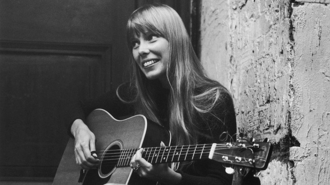 Joni Mitchell strums her guitar outside the Revolution club in London, circa 1968.