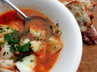 A bowl of fish stew with a chunk of bread on the side A bowl of fish stew with a chunk of bread on the side