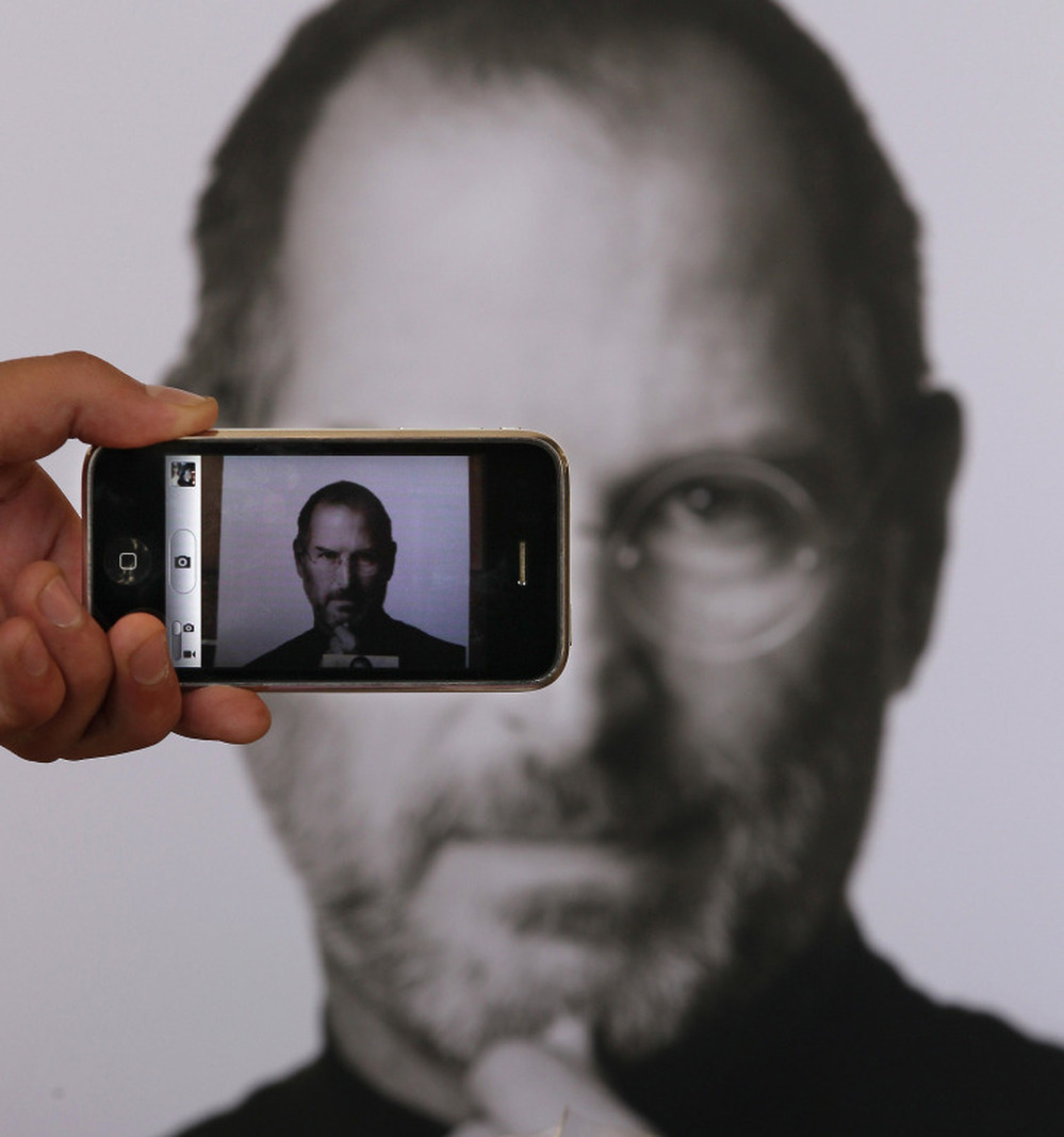 A photographer uses his iPhone to take a picture of a tribute to Apple co-founder Steve Jobs in front of an Apple store in London. 