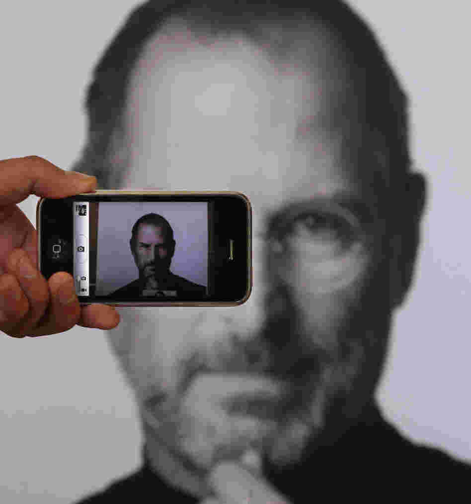 A photographer uses his iPhone to take a picture of a tribute to Apple co-founder Steve Jobs in front of an Apple store in London. 