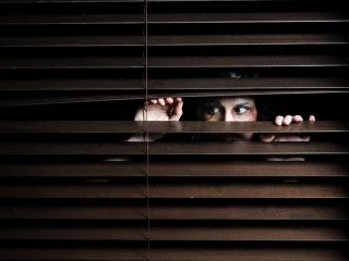 A woman looking through blinds. iStockphoto.com