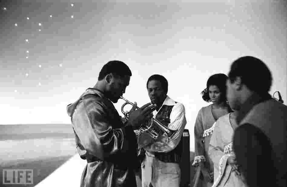 On the set of NBC's long-running "Kraft Music Hall" variety show, Frazier tests out a band member's trumpet.