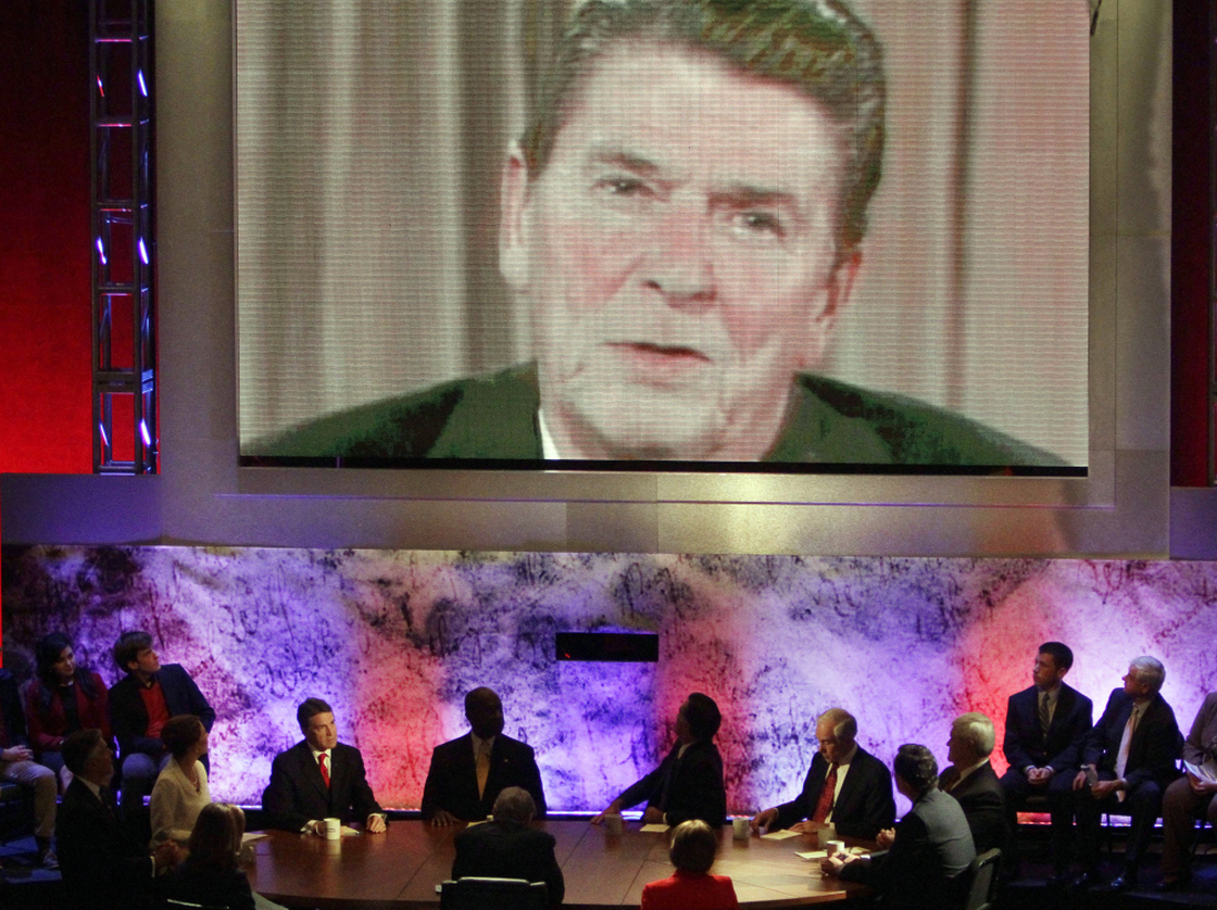 The eight Republican presidential candidates sitting at the table listen as a video of former President Ronald Reagan is played during a debate at Dartmouth College in Hanover, N.H., on Oct. 11. 