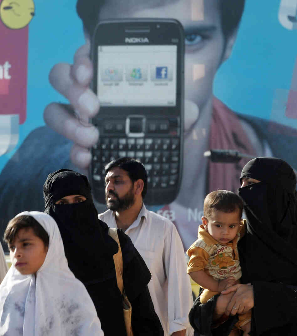 Pakistani families walk past an advertisement for a cellular telephone company in Rawalpindi.