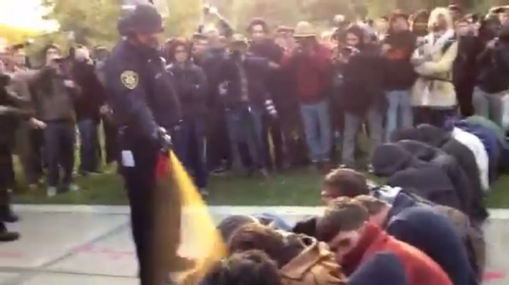 In this image made from video, a police officer uses pepper spray as he walks down a line of Occupy demonstrators sitting on the ground at the University of California, Davis on Friday, Nov. 18, 2011. 