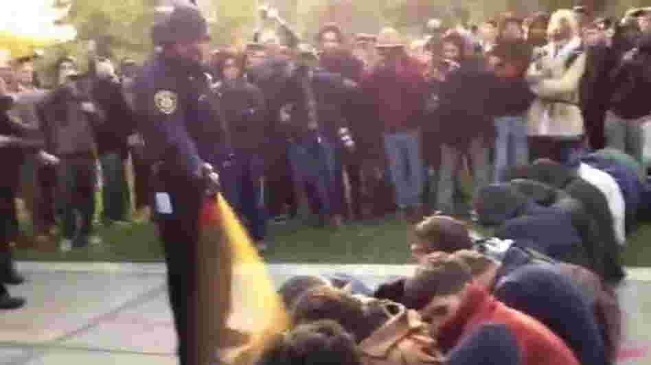 In this image made from video, a police officer uses pepper spray as he walks down a line of Occupy demonstrators sitting on the ground at the University of California, Davis on Friday, Nov. 18, 2011. 