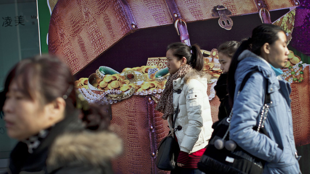 Chinese women walk past a billboard showing a box full of gold coins and jewelry, outside a shopping mall in Beijing on Thursday. Chinese leaders are scrambling to shore up flagging economic growth as exports weaken, abruptly reversing course after they spent two years struggling to cool an overheated expansion and surging inflation.