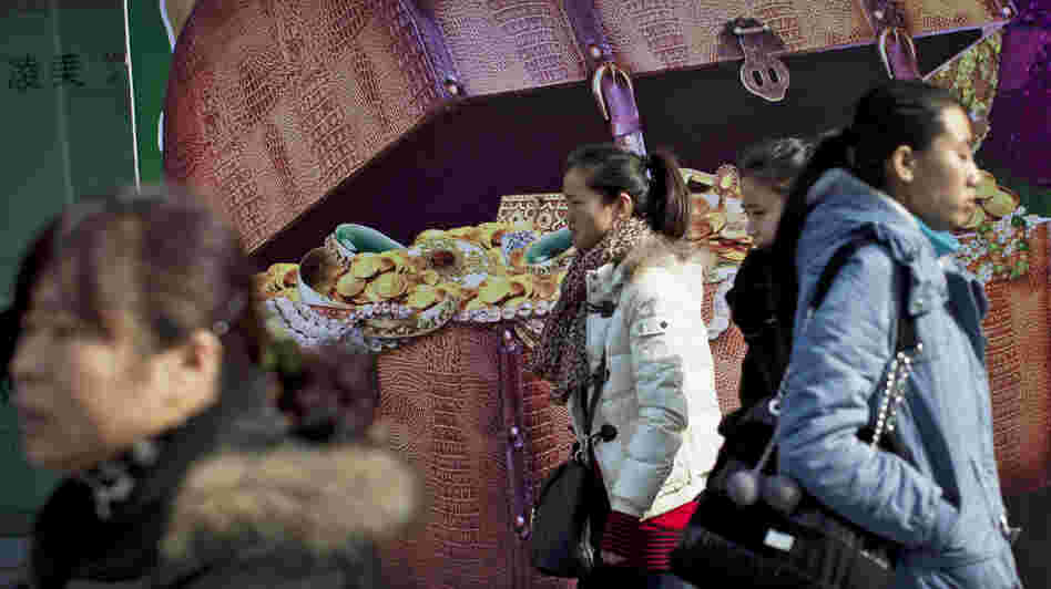 Chinese women walk past a billboard showing a box full of gold coins and jewelry, outside a shopping mall in Beijing on Thursday. Chinese leaders are scrambling to shore up flagging economic growth as exports weaken, abruptly reversing course after they spent two years struggling to cool an overheated expansion and surging inflation.