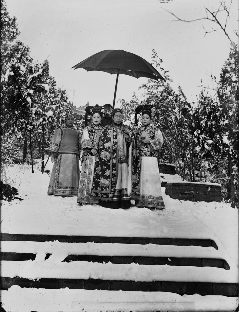 Cixi, accompanied by her attendants, stands in the snowy gardens of Wanshoushan (Longevity Hill), the central hill of the Summer Palace. The image is one of nine similar photographs that were most likely taken for the enjoyment of the empress and her attendants — not for any diplomatic purpose.
