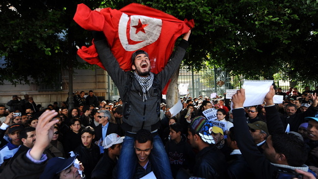 Tunisians protest outside the gates to the French Embassy in Tunis. Arab Spring began in Tunisia when a fruit vendor set himself on fire in protest in front of a government building.