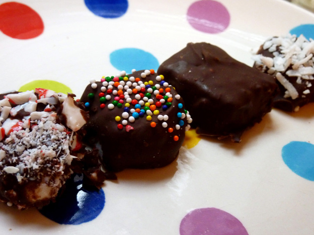 Marshmallows dipped in chocolate and various sprinkles sit on a polka-dot plate